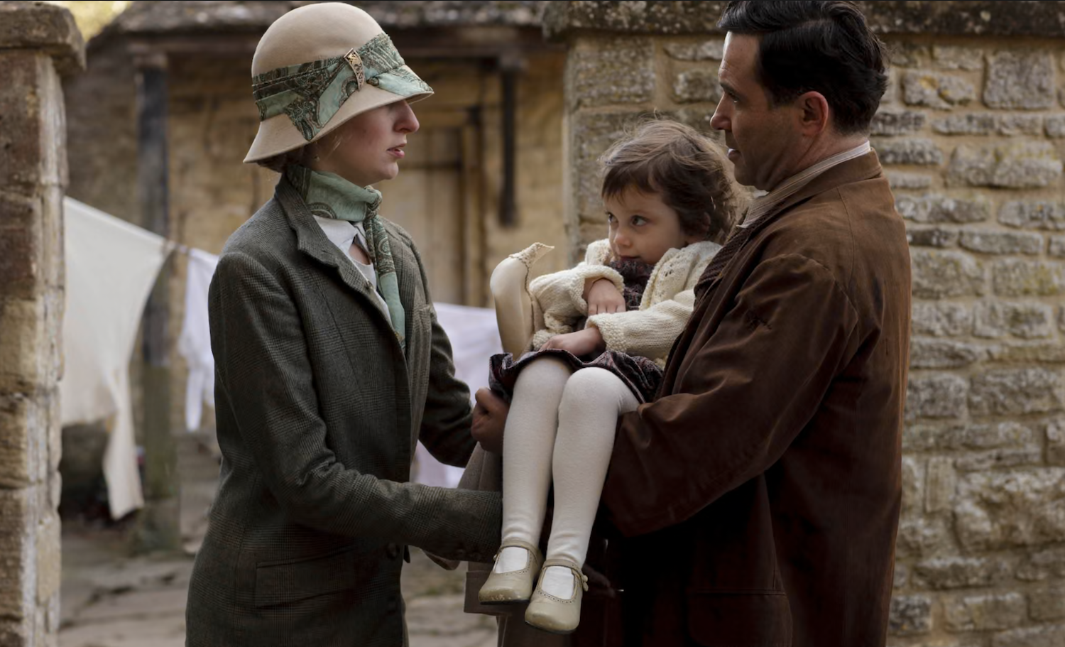 In a yard with laundry drying, Lady Edith (Laura Carmichael) hands over Marigold (Eva Samms) to Mr. Drewe (Andrew Scarborough). 