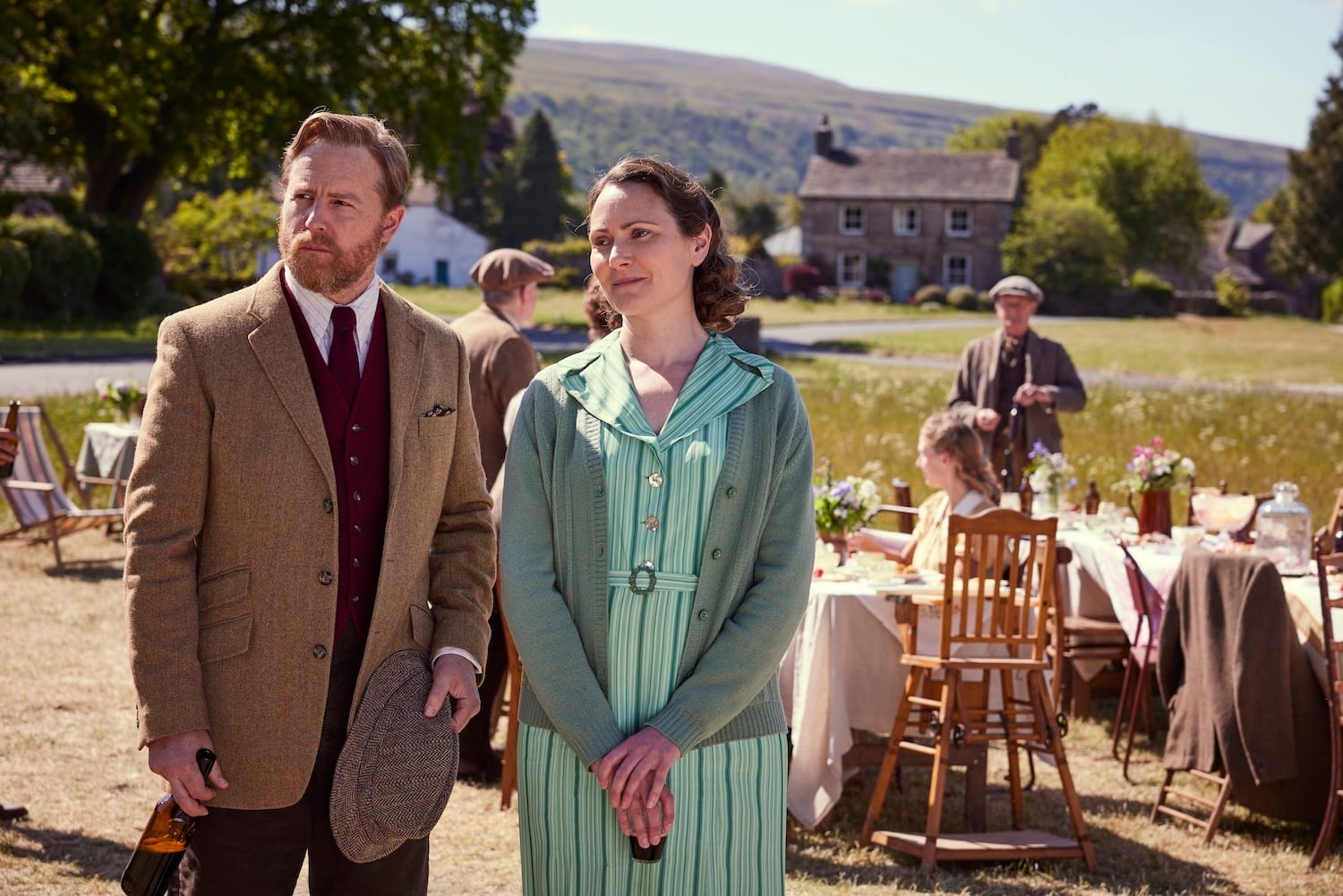 Siegfried Farnon (Samuel West) and Audrey Hall (Anna Madeley) stand in front of preparations for the party on the Green, but their expressions show their concern for Tristan who is missing. 