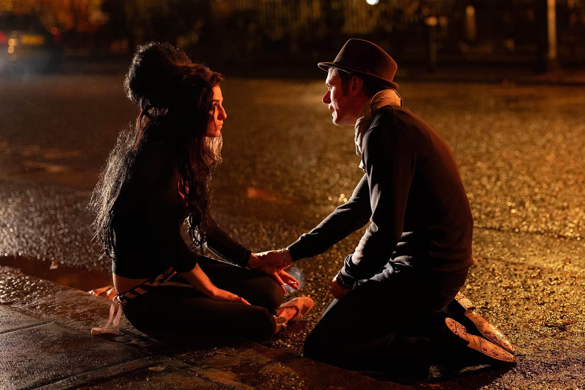 Marisa Abela as Amy Winehouse and Jack O'Connell as Blake Fielder-Civil sit in the middle of the street in 'Back to Black'