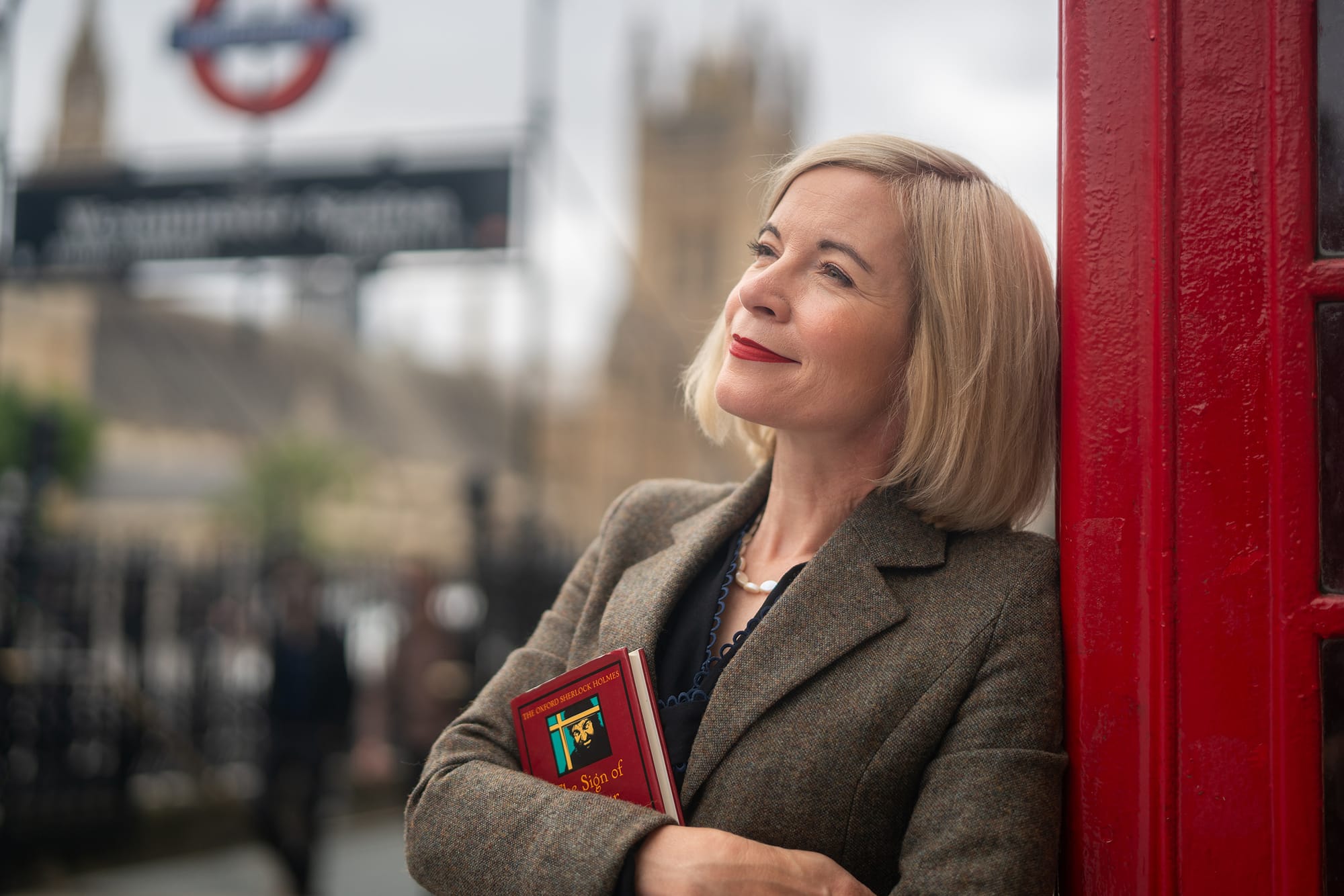 Lucy Worsley clutching a book and leaning against a red telephone box in front of Westminster in 'Lucy Worsley's Holmes vs. Doyle'